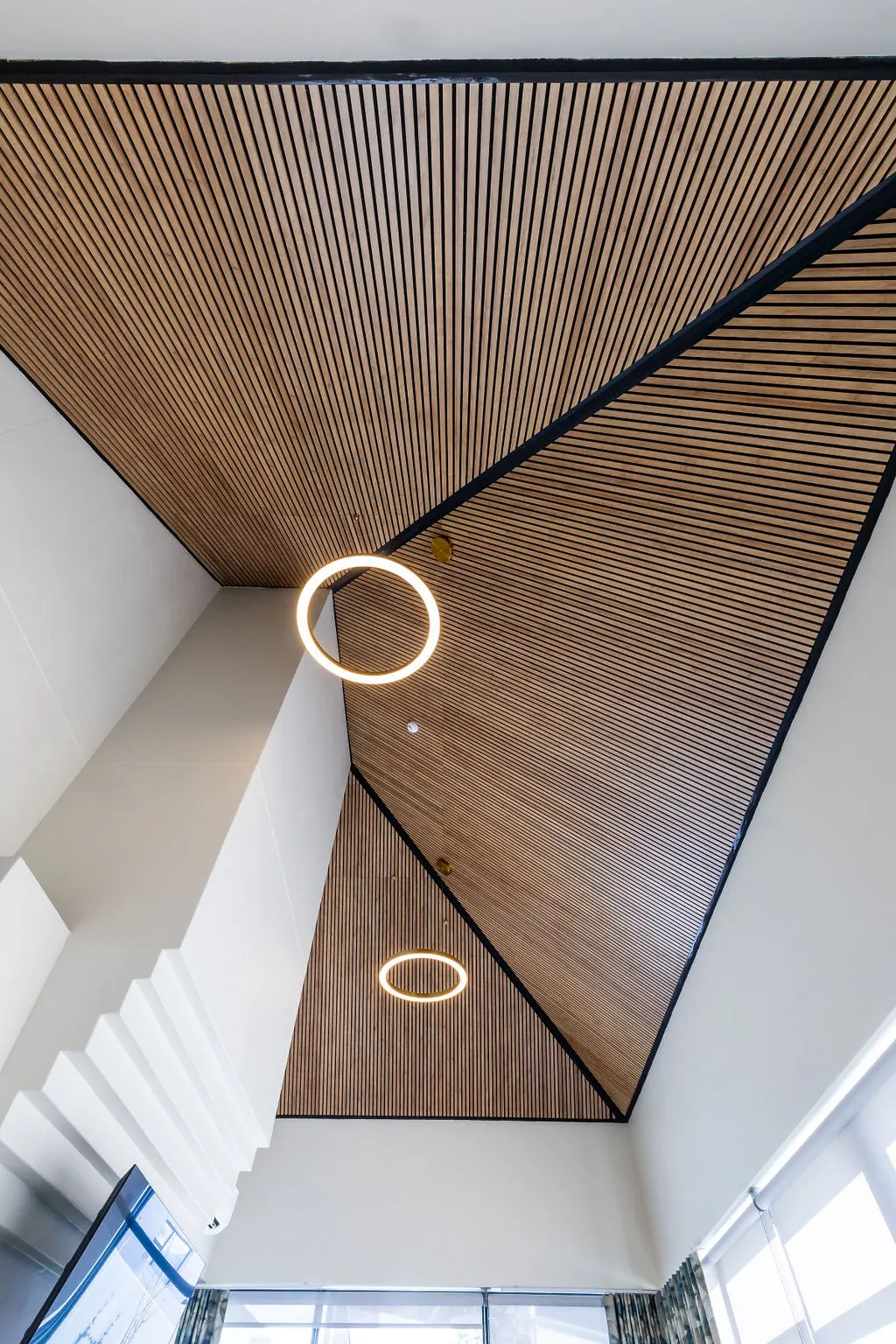 Geometric acoustic wood slat panel ceiling with ring pendant lights